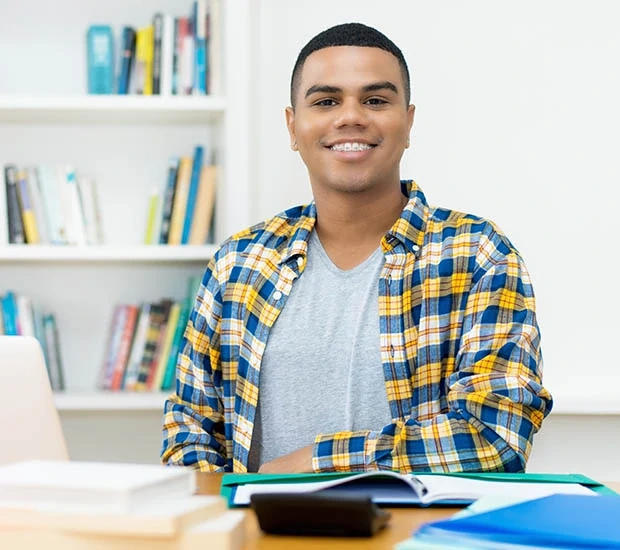 Smiling young man sitting at a desk with books.